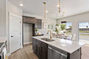 Kitchen featuring stainless steel dishwasher, a sink, light countertops, light wood-style flooring, and hanging light fixtures