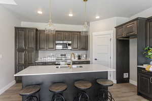 Kitchen with stainless steel appliances, a sink, light countertops, dark brown cabinets, and baseboards