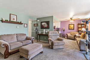 Living area featuring carpet floors, a ceiling fan, and a textured ceiling