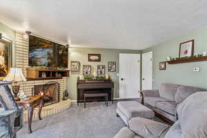 Living room featuring a textured ceiling, carpet, and a brick fireplace