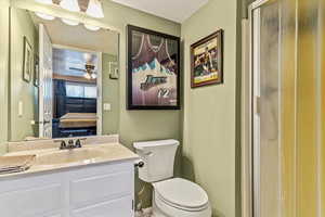Ensuite bathroom featuring toilet, vanity, ceiling fan, and an enclosed shower