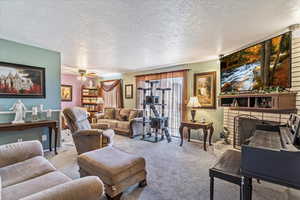 Carpeted living area with a textured ceiling, a ceiling fan, and a fireplace with raised hearth