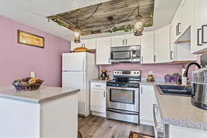 Kitchen with stainless steel appliances, a sink, light wood-type flooring, white cabinets, and light countertops