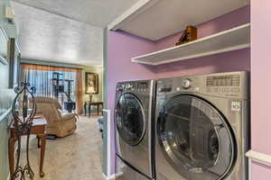 Laundry room featuring washing machine and clothes dryer, carpet flooring, and a textured ceiling