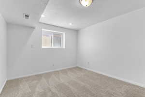 Carpeted empty room with a textured ceiling, baseboards, and recessed lighting