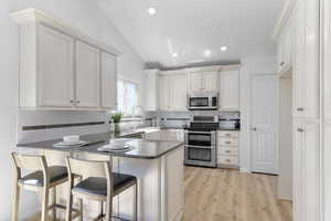 Kitchen featuring stainless steel appliances, a peninsula, lofted ceiling, tasteful backsplash, and dark stone countertops