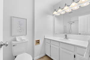 Full bathroom with toilet, vanity, a shower, wood finished floors, and baseboards