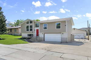 Raised ranch featuring brick siding, an attached garage, driveway, and a front yard