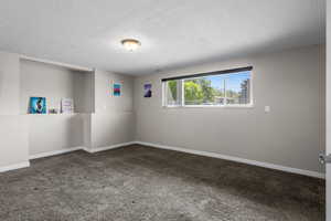 Carpeted spare room with a textured ceiling and baseboards