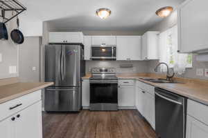 Kitchen with appliances with stainless steel finishes, a sink, dark wood finished floors, white cabinetry, and light countertops