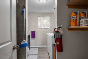 Laundry room with washing machine and dryer, a textured ceiling, baseboards, and a textured wall