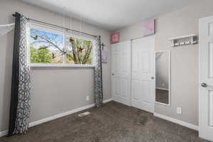 Unfurnished bedroom with dark colored carpet, a closet, and baseboards