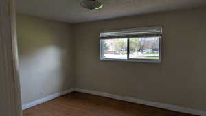Unfurnished room featuring baseboards, a textured ceiling, and wood finished floors