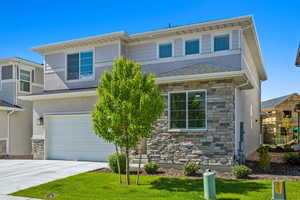 View of front facade with stone siding, an attached garage, stucco siding, driveway, and a front yard