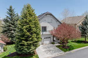 View of property hidden behind natural elements featuring stucco siding, a front lawn, a balcony, and concrete driveway