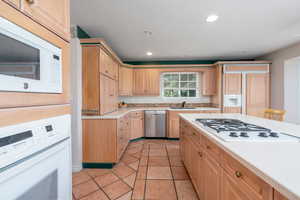 Kitchen with white appliances, light countertops, a sink, recessed lighting, and light brown cabinetry
