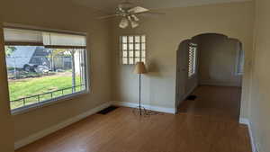 Spare room featuring wood finished floors, ceiling fan, arched walkways, and baseboards