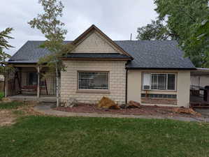 View of front of home with roof with shingles, a front lawn, and concrete block siding