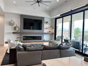 Living room featuring ceiling fan, healthy amount of natural light, a glass covered fireplace, light wood-style flooring, and recessed lighting