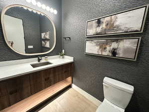Half bath featuring wood finished floors, toilet, vanity, and baseboards