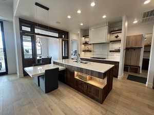 Kitchen featuring open shelves, a sink, light countertops, light wood-style floors, and a large island with sink