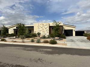 View of front of property with an attached garage, concrete driveway, stucco siding, and stone siding
