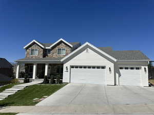 View of front of home with an attached garage, driveway, a porch, a front lawn, and stone siding
