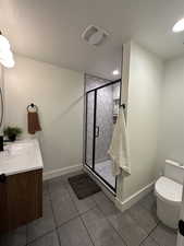 Bathroom with a textured ceiling, tile patterned floors, a stall shower, toilet, and vanity