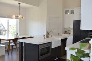 Kitchen with black appliances, light countertops, a sink, white cabinets, and hanging light fixtures