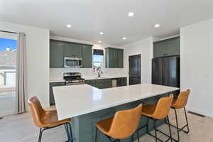 Kitchen with stainless steel appliances, light wood-style flooring, baseboards, green cabinets, and recessed lighting