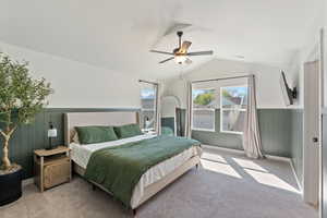 Bedroom featuring light carpet, lofted ceiling, a ceiling fan, and wainscoting