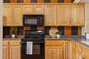 Kitchen featuring black appliances, light brown cabinetry, decorative backsplash, and dark countertops