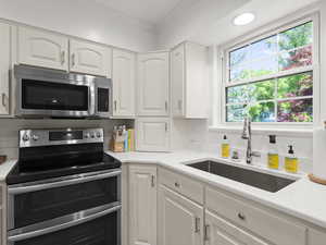Kitchen featuring appliances with stainless steel finishes, a sink, ornamental molding, decorative backsplash, and white cabinets