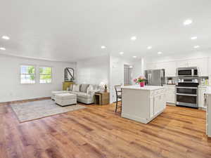Kitchen featuring stainless steel appliances, a center island, white cabinets, open floor plan, and light wood-style floors