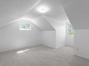 Bonus room with vaulted ceiling, light carpet, baseboards, and a textured ceiling