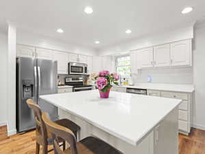 Kitchen featuring appliances with stainless steel finishes, a kitchen breakfast bar, crown molding, white cabinets, and light wood finished floors