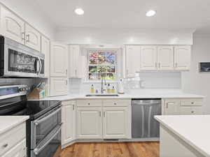 Kitchen with appliances with stainless steel finishes, a sink, crown molding, backsplash, and white cabinetry