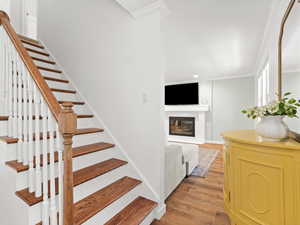Stairs featuring ornamental molding, wood finished floors, a glass covered fireplace, and recessed lighting