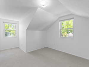 Bonus room featuring light carpet, vaulted ceiling, baseboards, and a textured ceiling