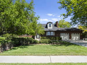 View of front of home with a chimney, a garage, driveway, and a front lawn