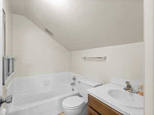 Bathroom with lofted ceiling, a garden tub, a textured ceiling, toilet, and vanity