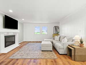Living room featuring wood finished floors, ornamental molding, a fireplace with flush hearth, recessed lighting, and baseboards