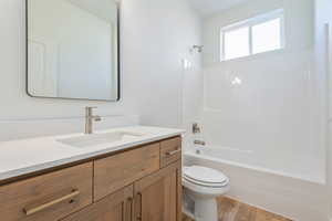 Full bathroom with toilet, wood finished floors, vanity, and washtub / shower combination