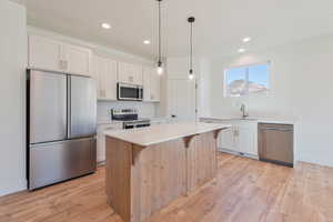 Kitchen with stainless steel appliances, a sink, light countertops, light wood-style flooring, and white cabinets