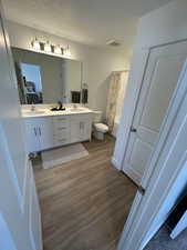 Ensuite bathroom featuring toilet, wood finished floors, double vanity, a textured ceiling, and shower / bath combination with curtain