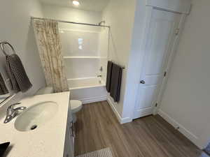 Bathroom featuring toilet, wood finished floors, vanity, shower / bath combination with curtain, and baseboards