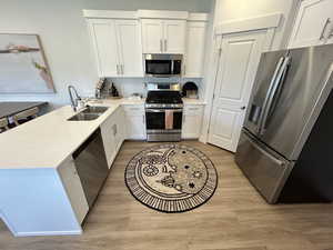 Kitchen with appliances with stainless steel finishes, light wood-style floors, a peninsula, white cabinetry, and a sink