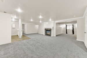Unfurnished living room featuring carpet floors, a fireplace with flush hearth, ornamental molding, and baseboards