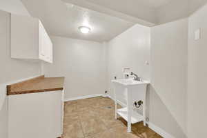 Laundry area with electric dryer hookup, hookup for a washing machine, a textured ceiling, baseboards, and cabinet space