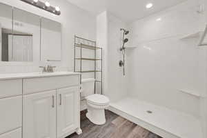 Full bathroom with toilet, wood finished floors, a shower, and vanity